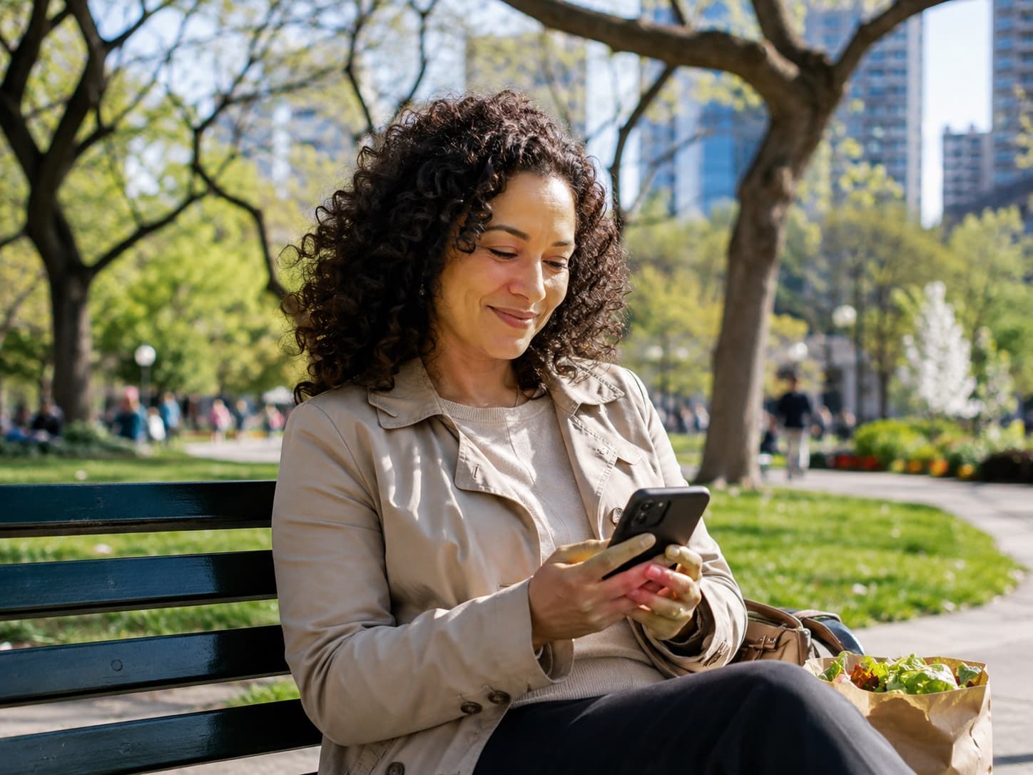 Woman smiling at her phone on a park bench, receiving a message from Buddi