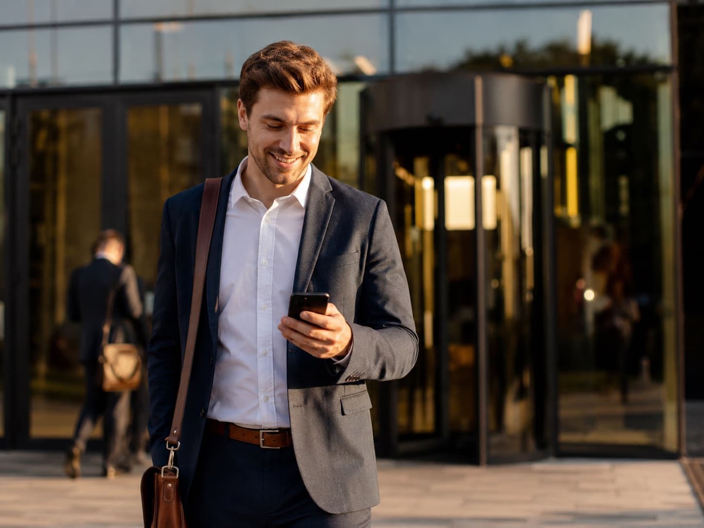 Man smiling at his phone outside his office building