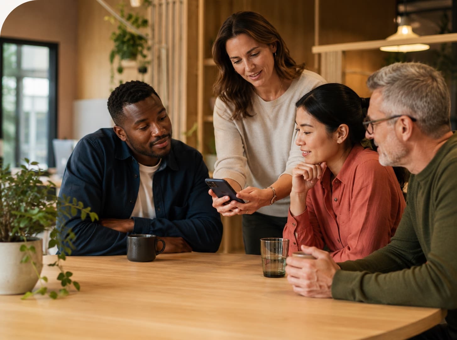 A group of colleagues gathered around a table looking at a phone together